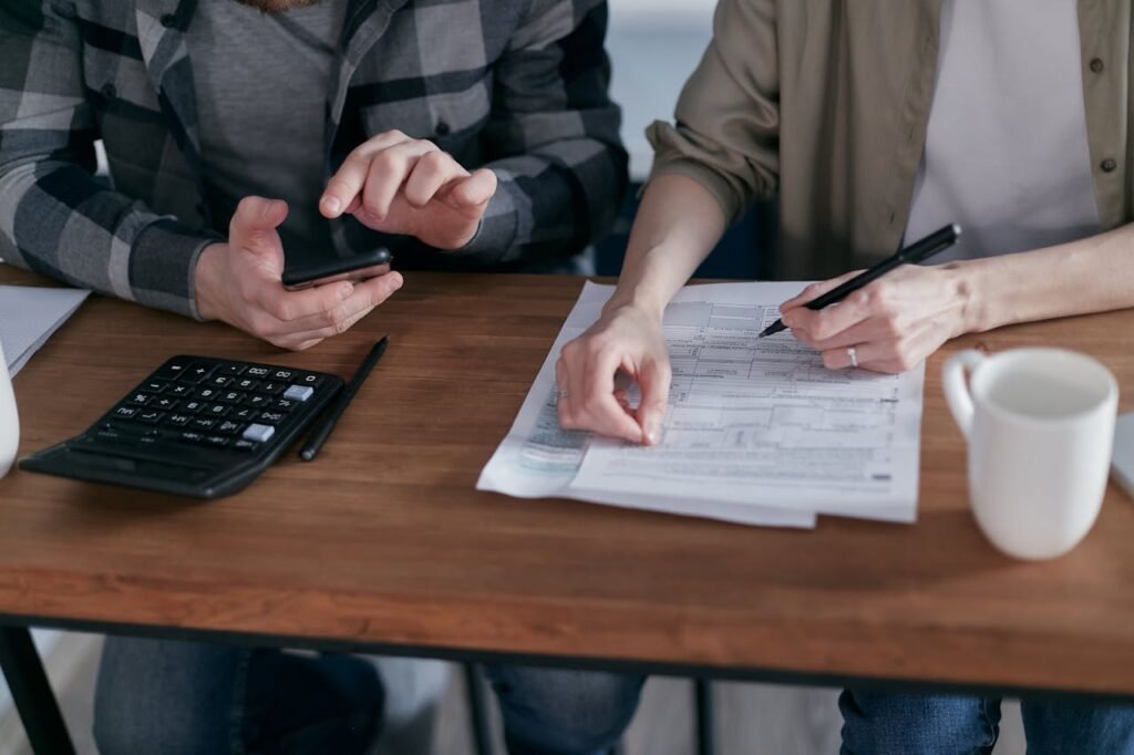 Two people working together on tax forms using a calculator at a wooden desk.